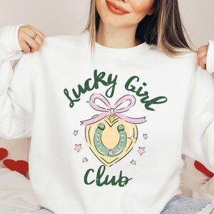 May include: White sweatshirt with a green and pink graphic design that says "Lucky Girl Club" with a horseshoe and a heart.