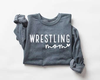 May include: A dark gray sweatshirt with the words "WRESTLING mom" printed in white. The sweatshirt is folded, with the sleeves rolled up. The text is in a bold, sans-serif font, with "mom" in a cursive script.
