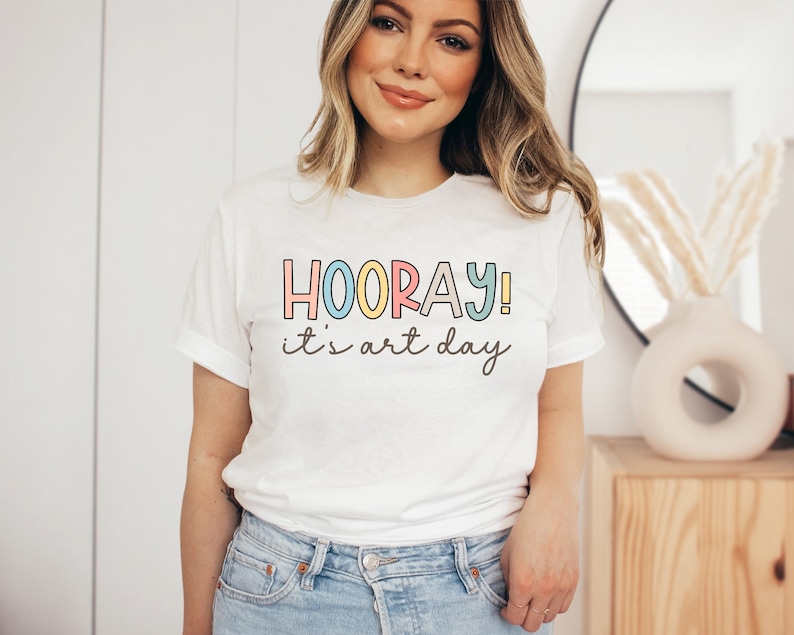 May include: White t-shirt with the text "HOORAY! it's art day" in colourful letters.
