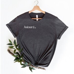 May include: A dark gray t-shirt with the text "Awkward" and a small heart on the front.