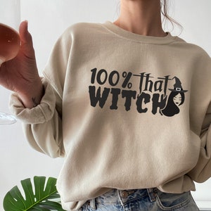 May include: A beige sweatshirt with the text "100% that WITCH" in black lettering. A black silhouette of a witch with a hat is next to the text.