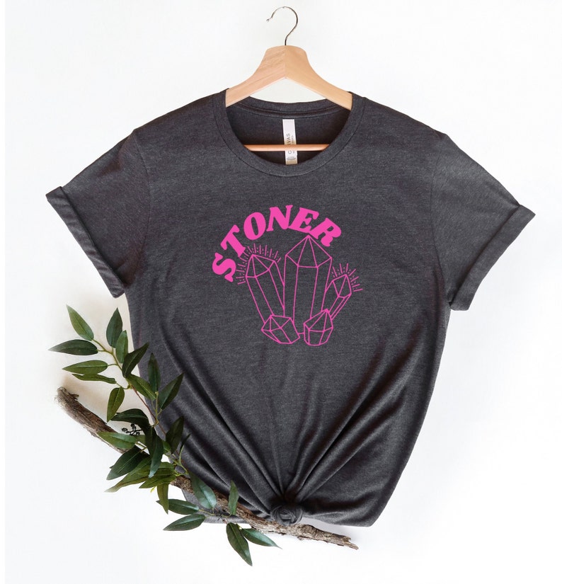 May include: A dark gray t-shirt with a pink graphic of crystals and the word "STONER" in pink.