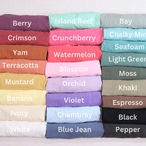 May include: A display of folded t-shirts in various colors, including Berry, Crimson, and Yam. Each shirt is labeled with its color name in white text. Other colors include Island Reef, Crunchberry, and Watermelon.