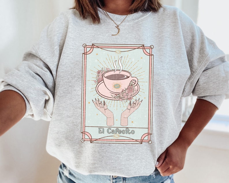 May include: Gray sweatshirt with a graphic of a coffee cup in a vintage tarot card style. The card reads "El Cafeito".