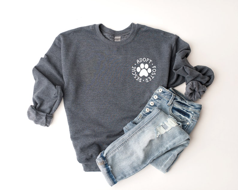 May include: A dark gray sweatshirt with a white paw print and the text "Adopt - Foster - Rescue" around it. The sweatshirt is paired with light blue jeans.