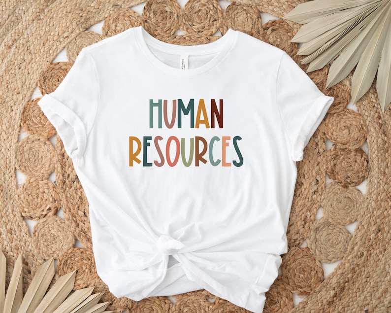 May include: White t-shirt with the text "HUMAN RESOURCES" in colorful, stylized letters.