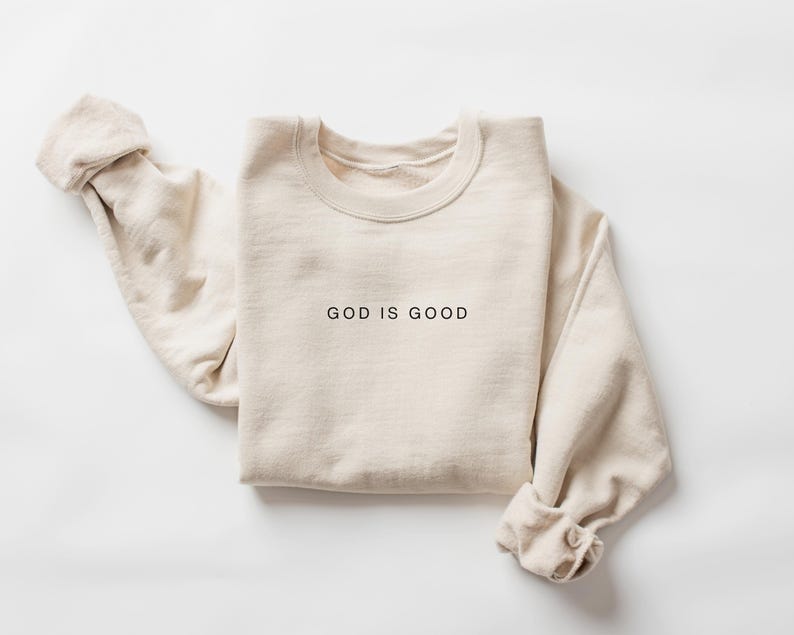 K&ouml;nnte beinhalten: Ein beiger Pullover mit dem Aufdruck "GOD IS GOOD" auf der Vorderseite.