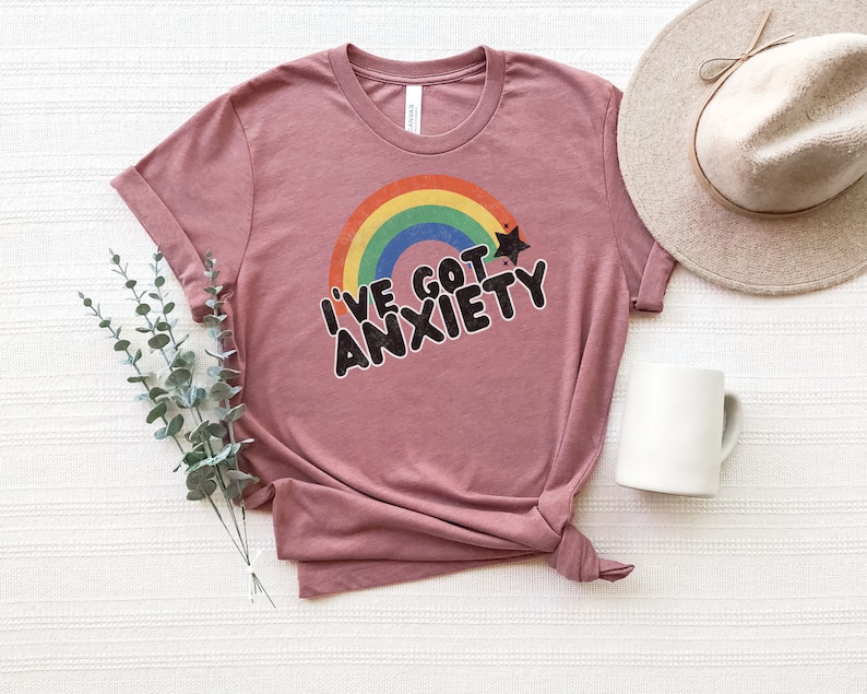 May include: A mauve t-shirt with a rainbow and a star graphic. The text "I've got anxiety" is printed in black on the shirt.