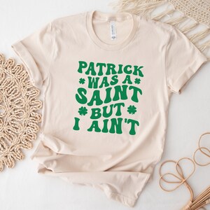 May include: A beige t-shirt with a green graphic that reads "Patrick was a saint but I ain't".