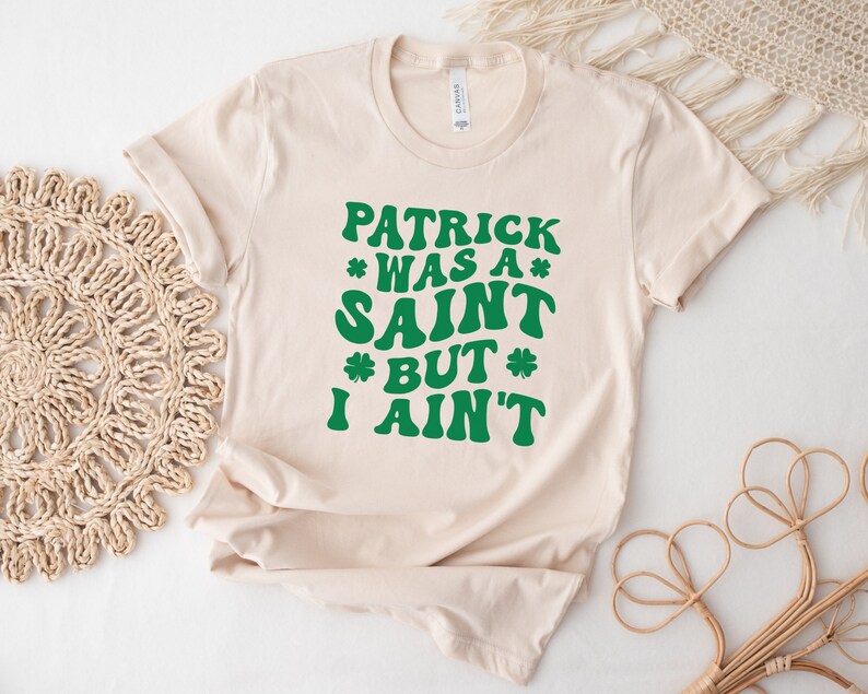 May include: A beige t-shirt with a green graphic that reads "Patrick was a saint but I ain't".