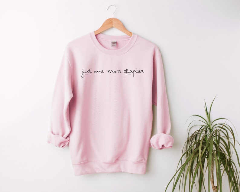 May include: A pink sweatshirt with the text "just one more chapter" in black script.