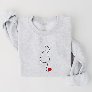 Peut inclure: Un sweat-shirt gris avec un dessin au trait noir d'un chat avec un c&oelig;ur rouge au bout de sa queue.