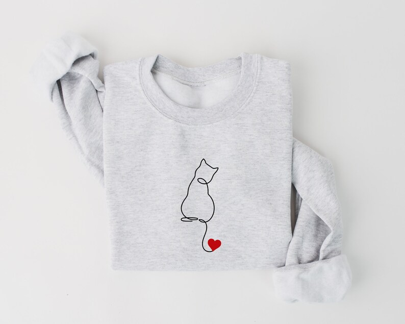 Peut inclure: Un sweat-shirt gris avec un dessin au trait noir d'un chat avec un c&oelig;ur rouge au bout de sa queue.