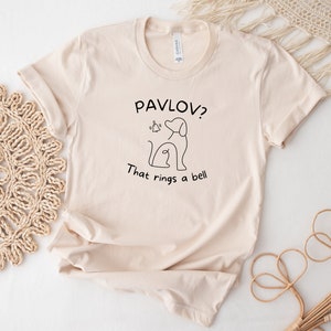 May include: A beige t-shirt with a black line drawing of a dog and the text "Pavlov? That rings a bell."