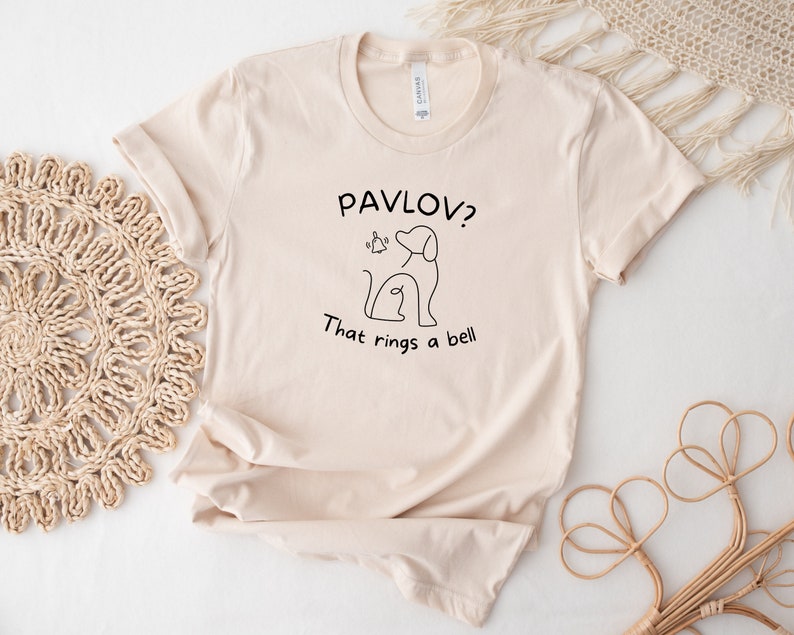 May include: A beige t-shirt with a black line drawing of a dog and the text "Pavlov? That rings a bell."