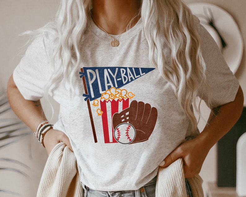 May include: A gray t-shirt with a graphic of a baseball glove, popcorn, and a pennant that says "PLAY-BALL".