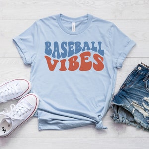 May include: A light blue t-shirt with the text "Baseball Vibes" in a retro font. The text is in blue and red.