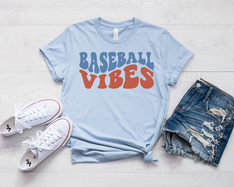 May include: A light blue t-shirt with the text "Baseball Vibes" in a retro font. The text is in blue and red.