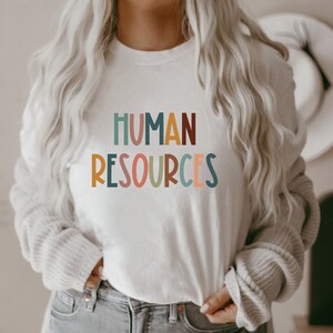 May include: A white t-shirt with the text "HUMAN RESOURCES" in colorful, stylized letters.