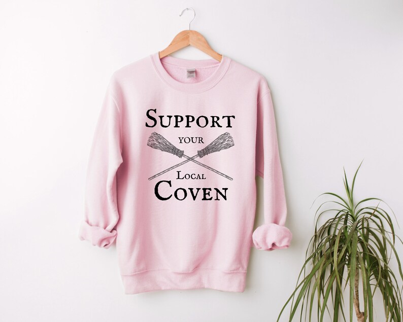 May include: Pink sweatshirt with the text "Support Your Local Coven" and a graphic of two crossed brooms.