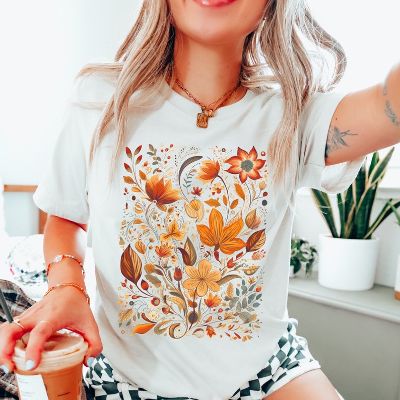 May include: White t-shirt with a floral print featuring yellow, orange, and brown flowers and leaves.