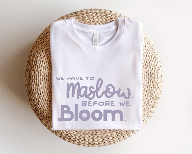 May include: White t-shirt with the text "We have to Maslow before we Bloom." in purple lettering.