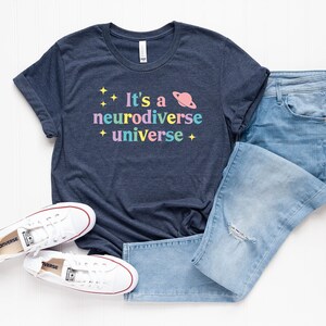 Pu&ograve; includere: Una maglietta blu navy con il testo "It's a neurodiverse universe" in colori arcobaleno con stelle e una grafica di un pianeta.