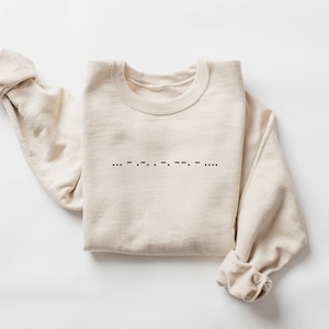 May include: A beige sweatshirt with a black design of braille dots on the front. The braille dots spell out the word "love".