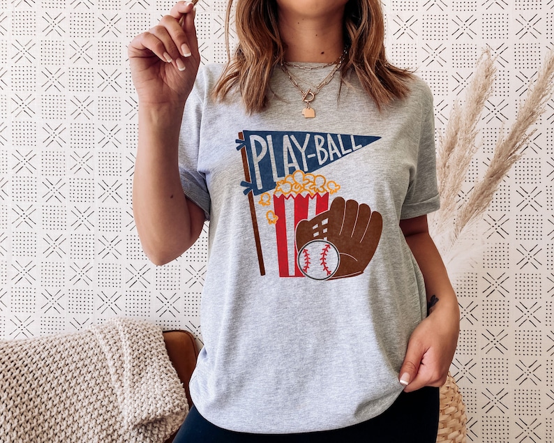 May include: Gray t-shirt with a graphic of a baseball glove, popcorn, and a pennant that says "Play-Ball".