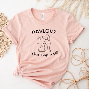 May include: A pink t-shirt with a black graphic of a dog and a bell with the text "Pavlov? That rings a bell."