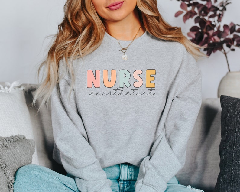 May include: A gray sweatshirt with the text "NURSE anesthetist" in colorful letters. The letters are outlined in black and have a rounded, playful font.