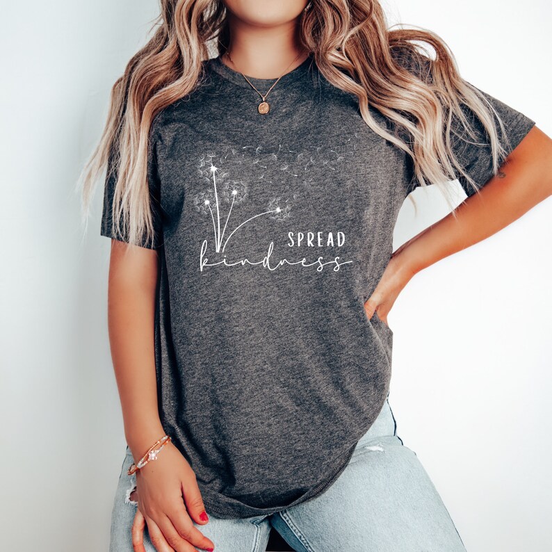 K&ouml;nnte beinhalten: Ein dunkelgraues T-Shirt mit einem wei&szlig;en L&ouml;wenzahnmuster und dem Text "SPREAD kindness".