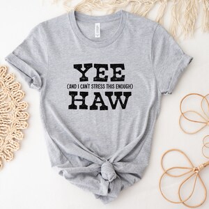 Op de afbeelding: Grijs T-shirt met een zwarte afbeelding met de tekst "Yee (and I can't stress this enough) Haw".