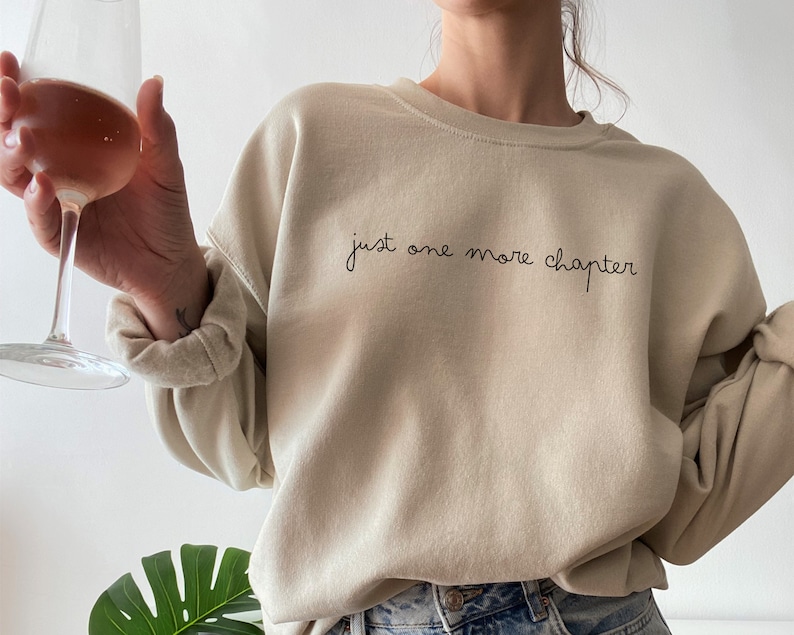 May include: A beige sweatshirt with the text "just one more chapter" in black script.