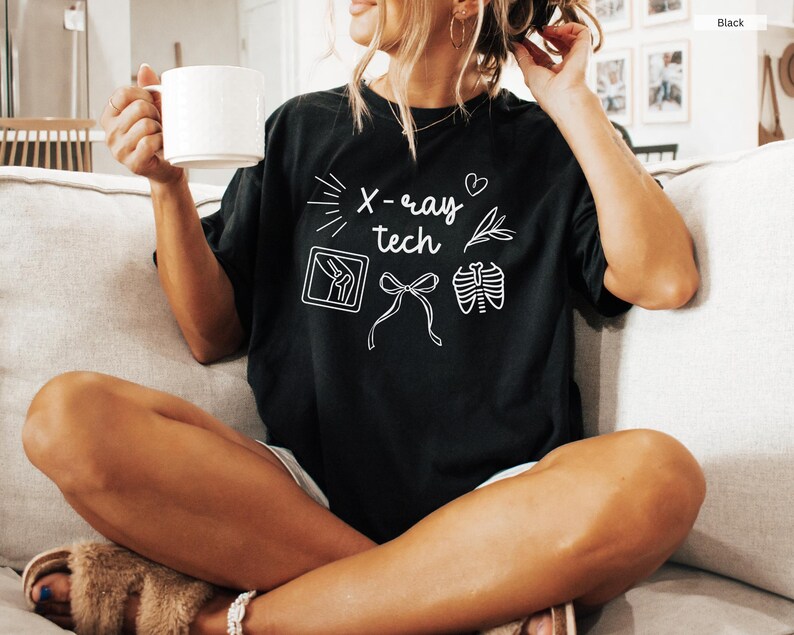 K&ouml;nnte beinhalten: Ein schwarzes T-Shirt mit wei&szlig;em Text, der "X-ray tech" lautet und Illustrationen einer R&ouml;ntgenaufnahme eines Knies, einer Schleife und einer R&ouml;ntgenaufnahme eines Brustkorbs enth&auml;lt.