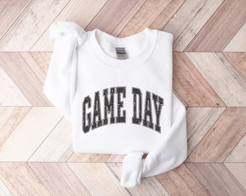 May include: White sweatshirt with the text "GAME DAY" in black, distressed lettering.