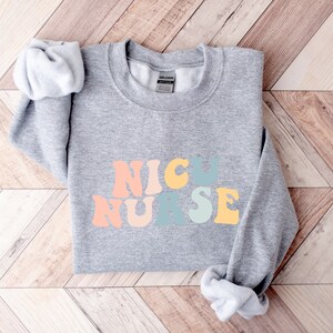May include: Grey sweatshirt with the words "NICU NURSE" in rainbow coloured letters.