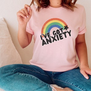 May include: A pink t-shirt with a rainbow and a star graphic. The text on the shirt reads "I've got anxiety".