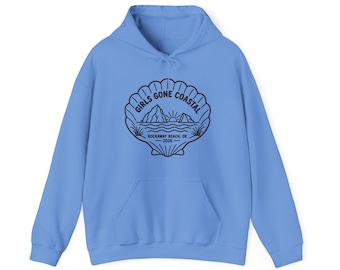 May include: A light blue hooded sweatshirt featuring a black graphic of a seashell containing a coastal scene with mountains, a sun, and waves. The text reads GIRLS GONE COASTAL, ROCKAWAY BEACH, OR, and 2026. It has long sleeves and a front pocket.