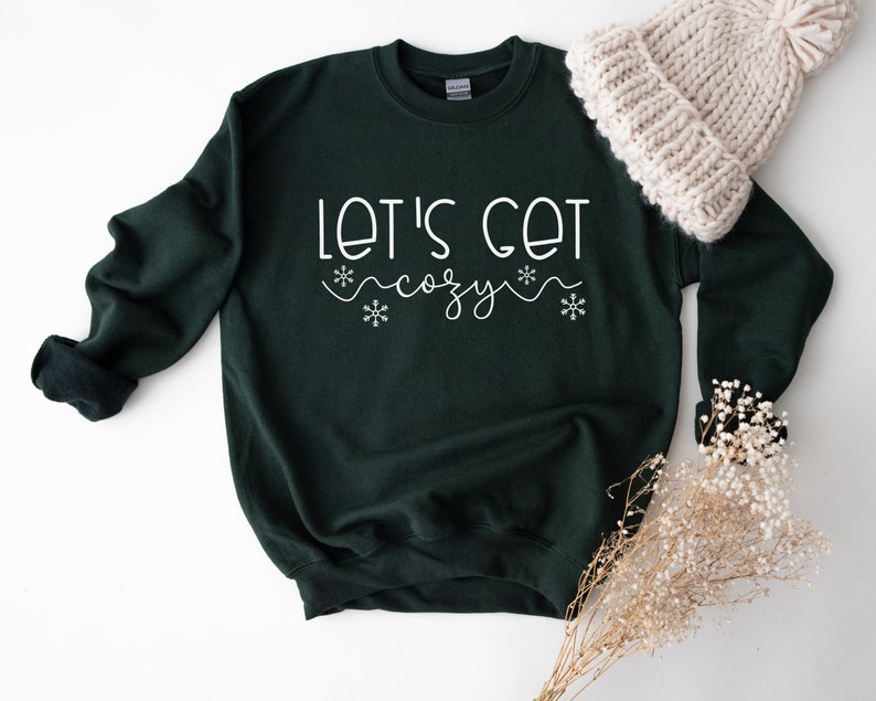 May include: A dark green sweatshirt with the text "Let's get cozy" in white lettering with snowflake accents.