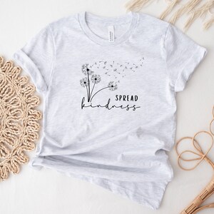 K&ouml;nnte beinhalten: Ein graues T-Shirt mit einer schwarzen L&ouml;wenzahndruck und dem Text "SPREAD kindness".