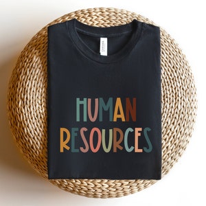 May include: Black t-shirt with the text "HUMAN RESOURCES" in colorful, stylized letters.