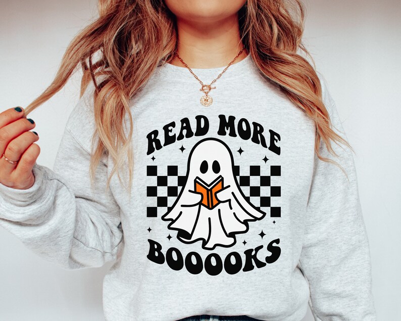 May include: A gray sweatshirt with a white ghost holding a book and the text "Read More Booooks" in black with a checkered pattern behind the ghost.