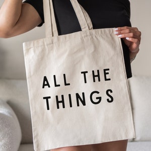 May include: A white canvas tote bag with black text that reads "ALL THE THINGS".
