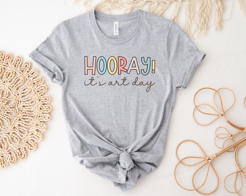 May include: Grey t-shirt with the text "HOORAY! it's art day" in colourful letters.