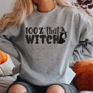May include: A gray sweatshirt with the text "100% that WITCH" and a black silhouette of a witch wearing a hat.