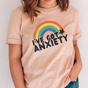 May include: A pink t-shirt with a rainbow and a star graphic. The text on the shirt reads "I've got anxiety".