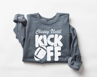 May include: A dark heather gray long-sleeve crewneck sweatshirt featuring white distressed text that reads Classy Until KICK OFF, with a graphic of an American football replacing the letter I in the word KICK.