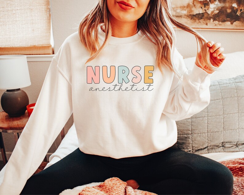 May include: White sweatshirt with the text "NURSE anesthetist" in colorful letters. The letters are outlined in black.