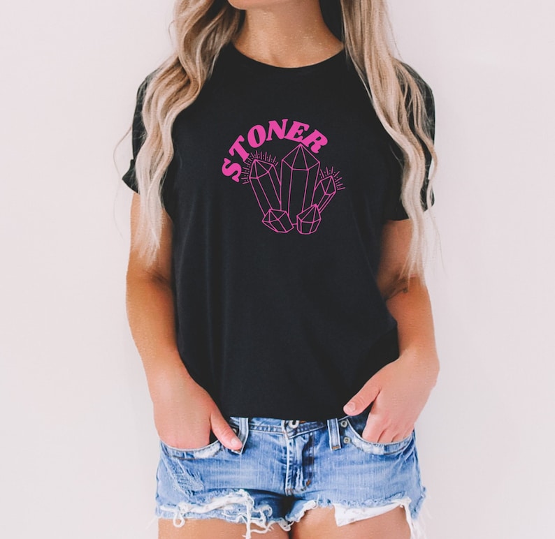 May include: A black t-shirt with a pink graphic of crystals and the word "STONER" in pink retro lettering.